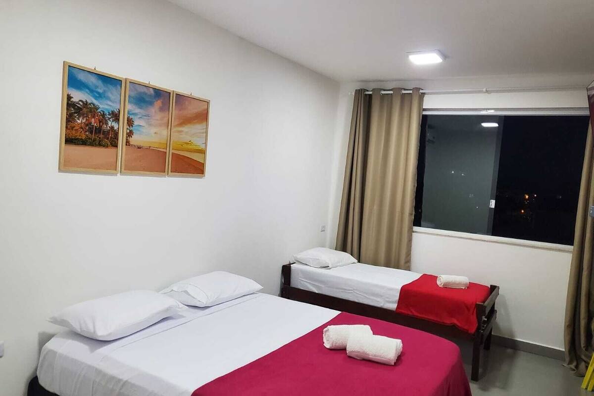 A hotel room with two single beds, a window with curtains, and a painting on the wall.