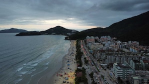 A coastal cityscape with a beach, buildings, and a hilly backdrop. - Apartamentos Casa Da Pedra (Ubatuba)