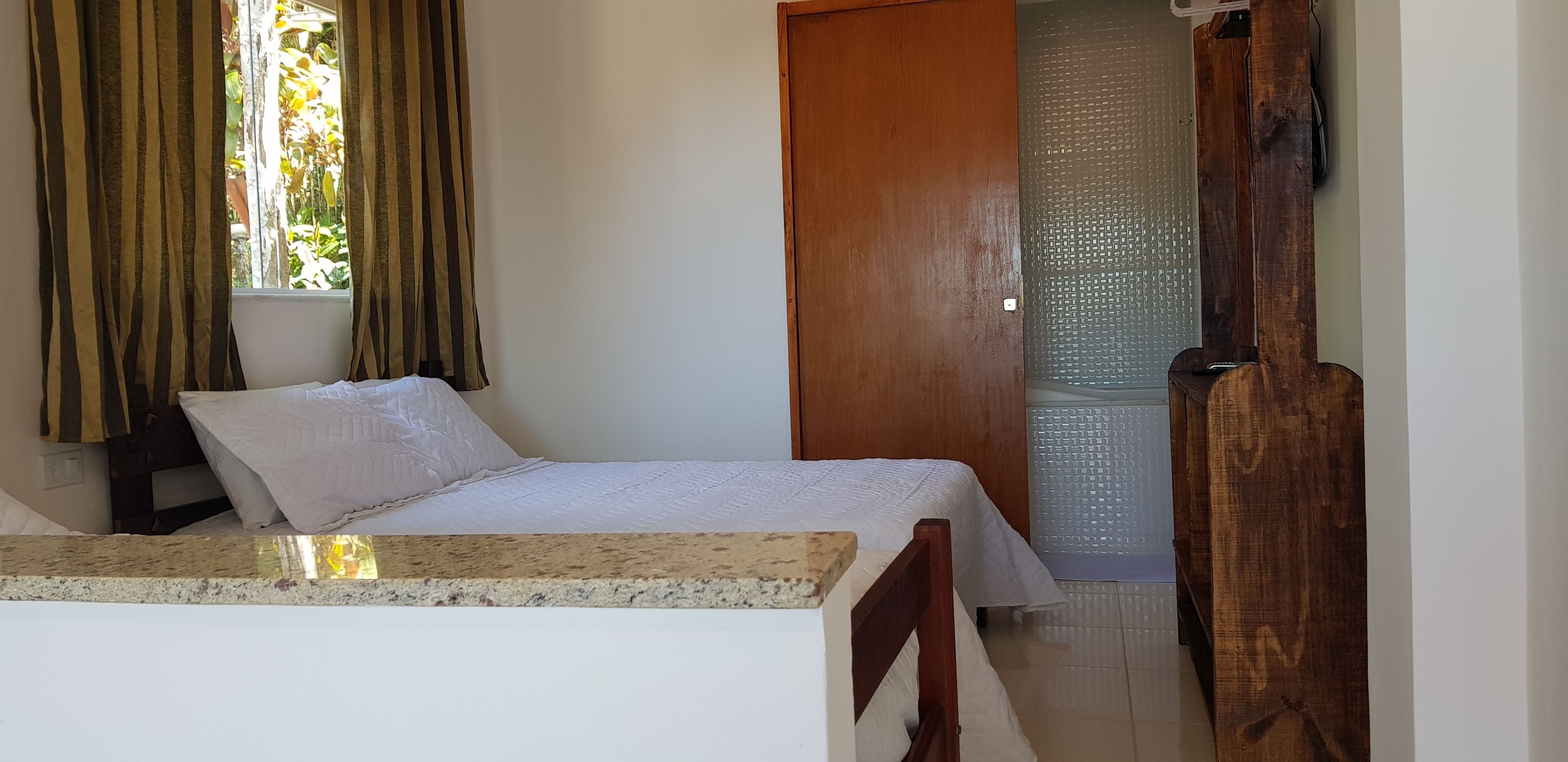 A bedroom with a bed, a wooden door, a window with curtains, and a small table.
