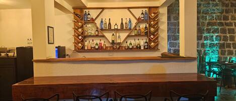 A bar area with a wooden counter and multiple shelves of liquor bottles. There are four chairs in front of the bar.