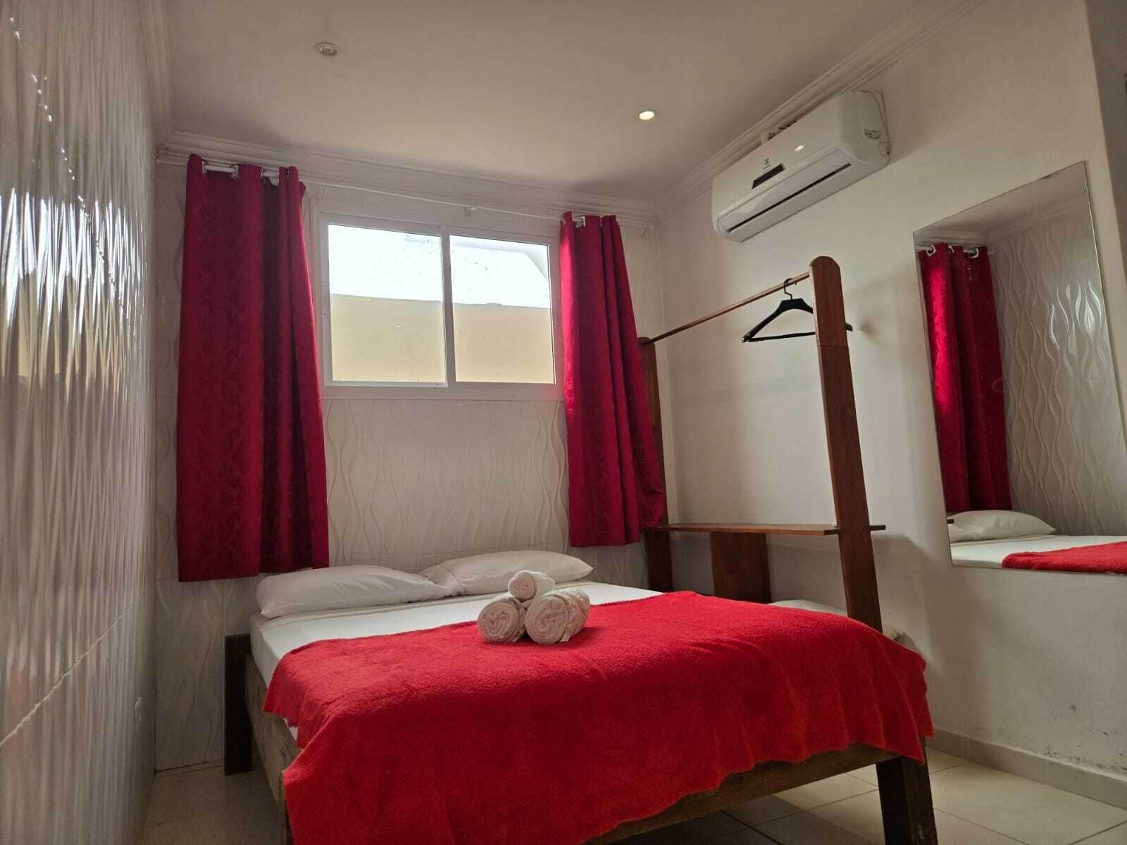 Una habitación pequeña y bien iluminada con una cama, un espejo y un equipo de aire acondicionado.