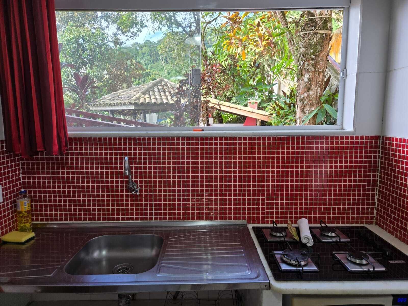 A kitchen with a red tiled backsplash, a stainless steel sink, and a gas stove.