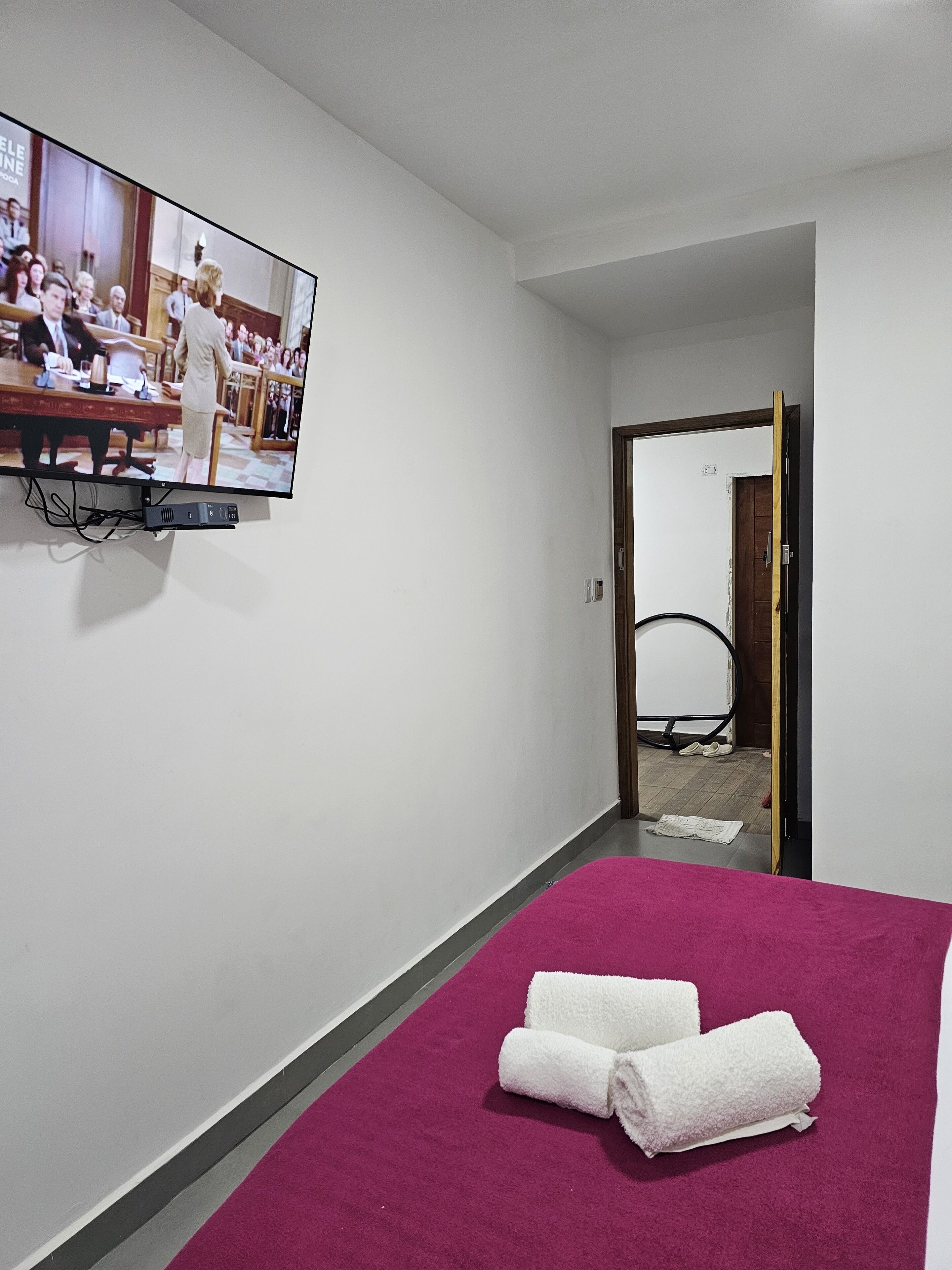 Een hotelkamer met een bed, een aan de muur bevestigde televisie en een deur naar een andere kamer.