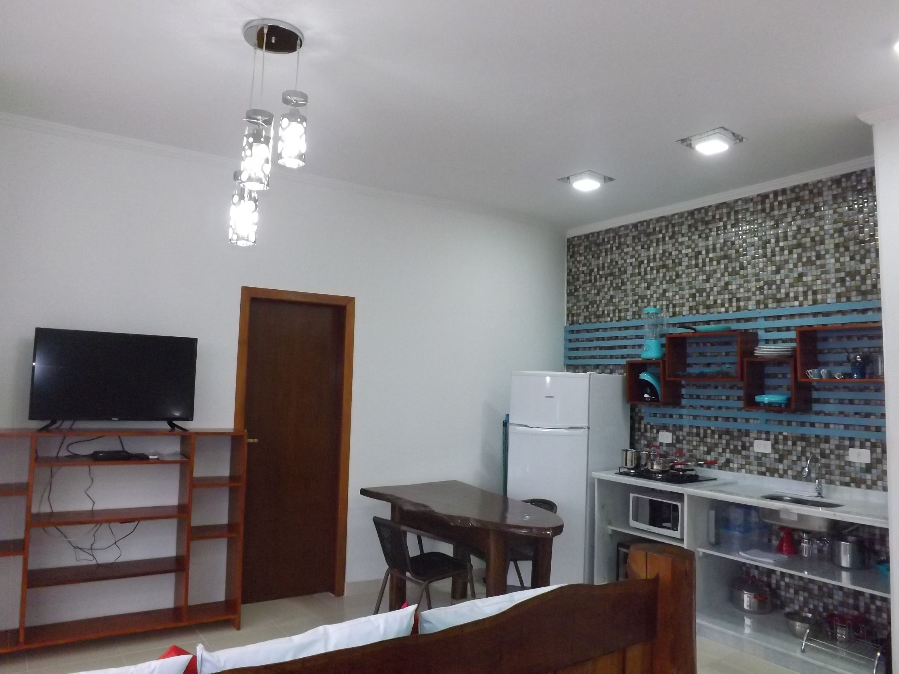 A compact kitchen with a refrigerator, a dining table with chairs, a TV on a stand, and a patterned backsplash.