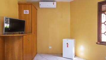 A room with a TV on a wooden cabinet, a white refrigerator, and an air conditioner on the wall.