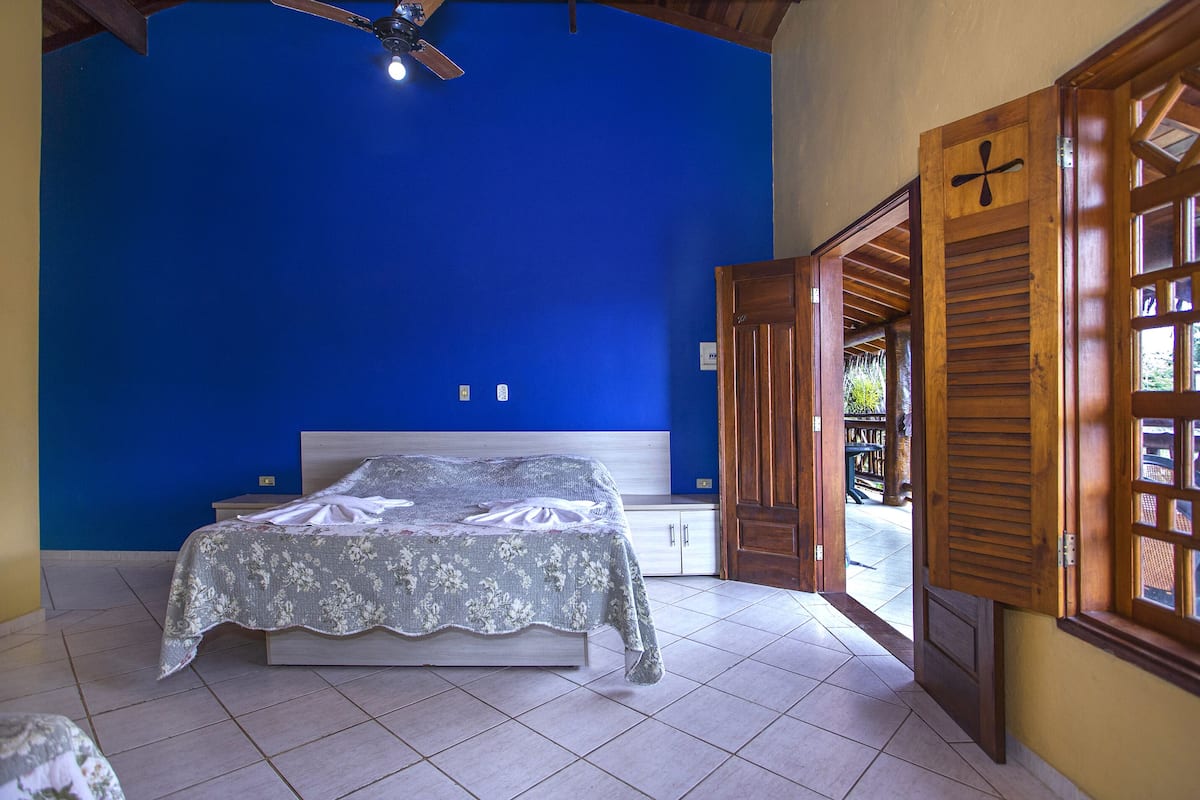 A bedroom with a bed, a ceiling fan, and a view of the outside through an open door.