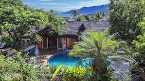Un resort tropical con piscina rodeada de exuberante vegetación y vista a la montaña.