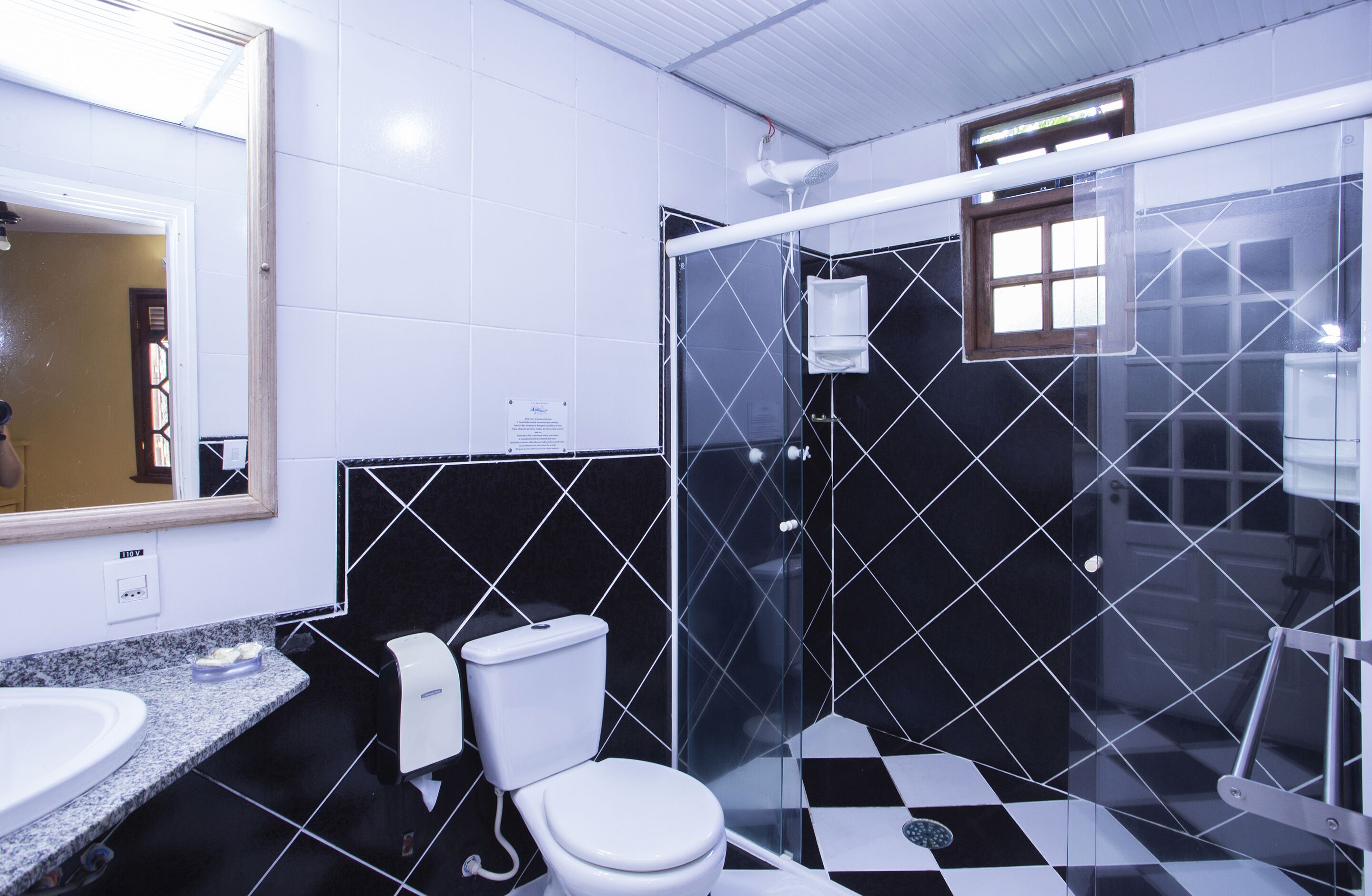 Un baño con inodoro blanco, lavamanos y ducha con mampara de vidrio.