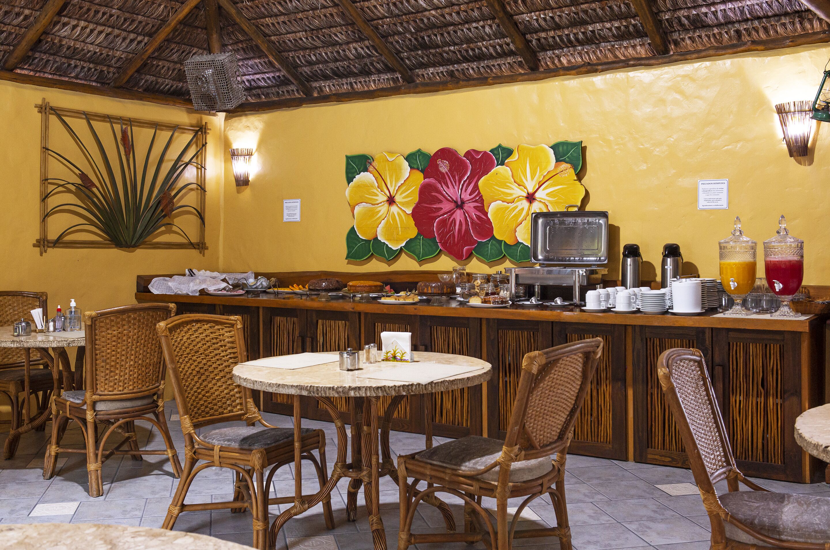 A restaurant with wicker chairs, a bar area with a fruit-themed mural, and a tiled floor.