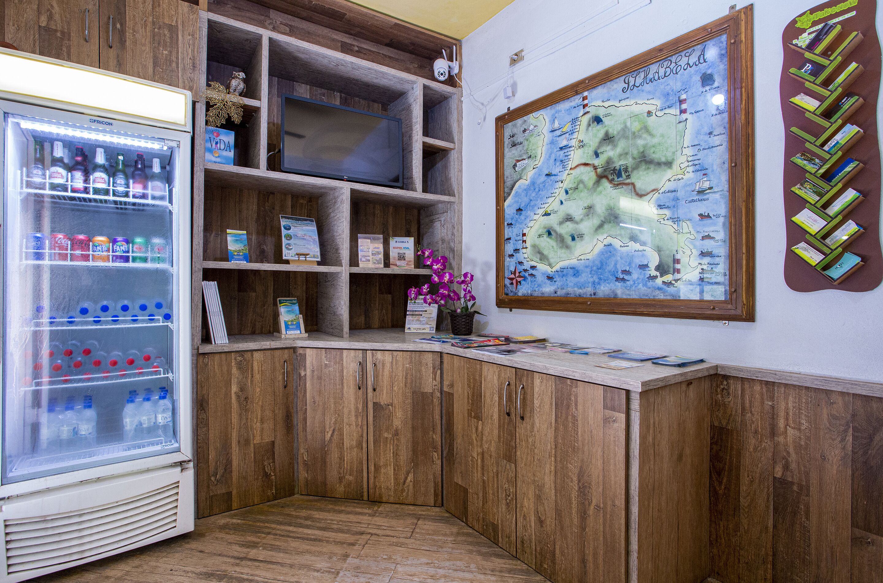 Un racó d'una habitació amb un frigorífic, prestatges de fusta, un mapa i una petita planta.