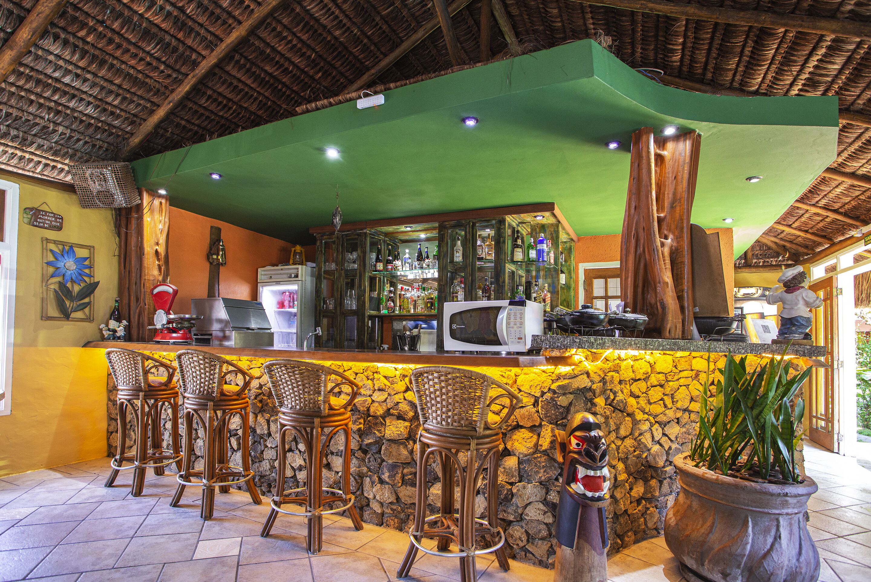A bar area with a stone wall, wooden bar stools, a microwave, and a potted plant.