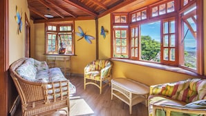 Una habitación con muebles de mimbre, ventanas amplias y vistas al exterior.