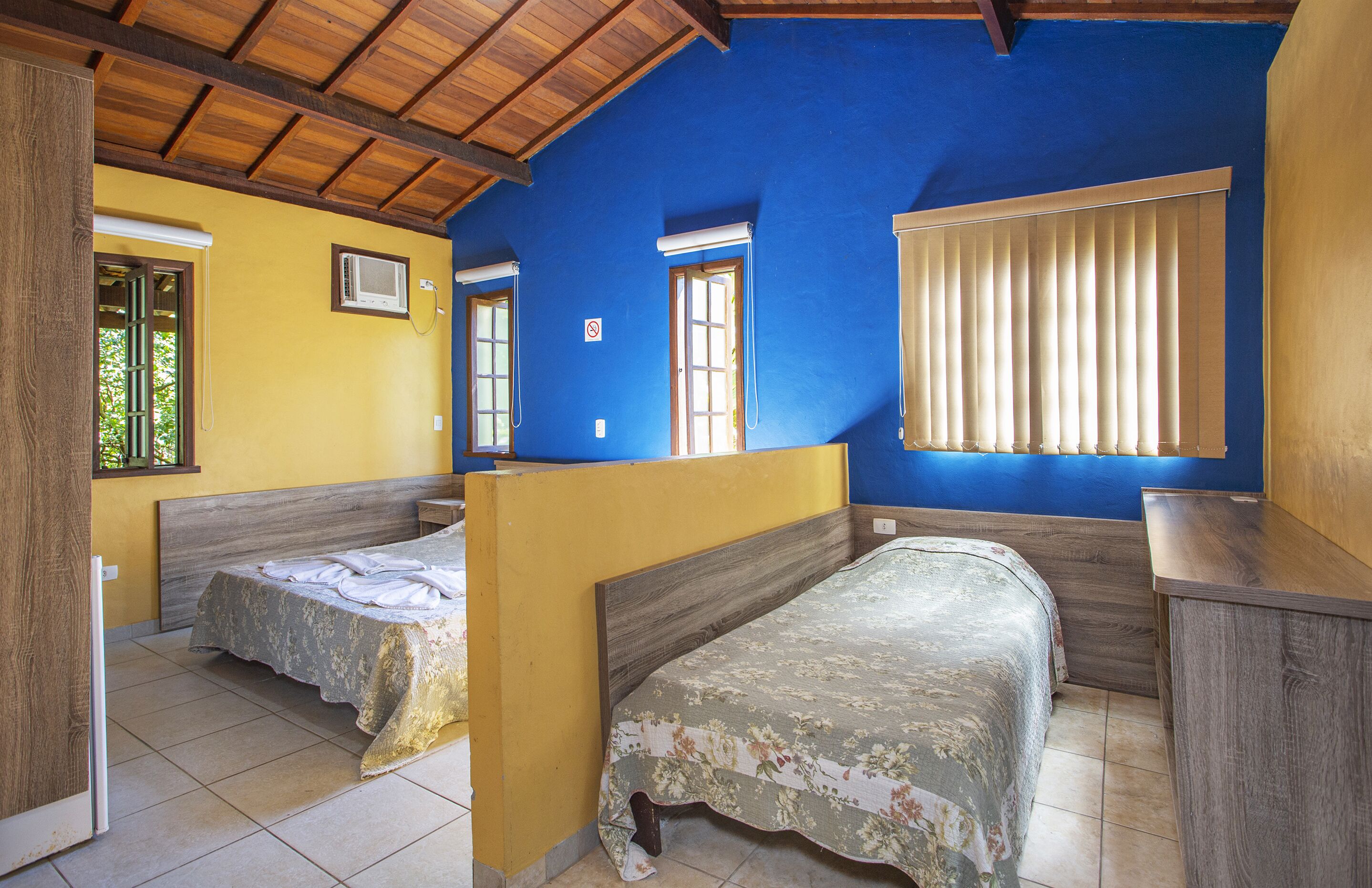 Una habitación con dos camas individuales, techo de madera y ventana con persianas.
