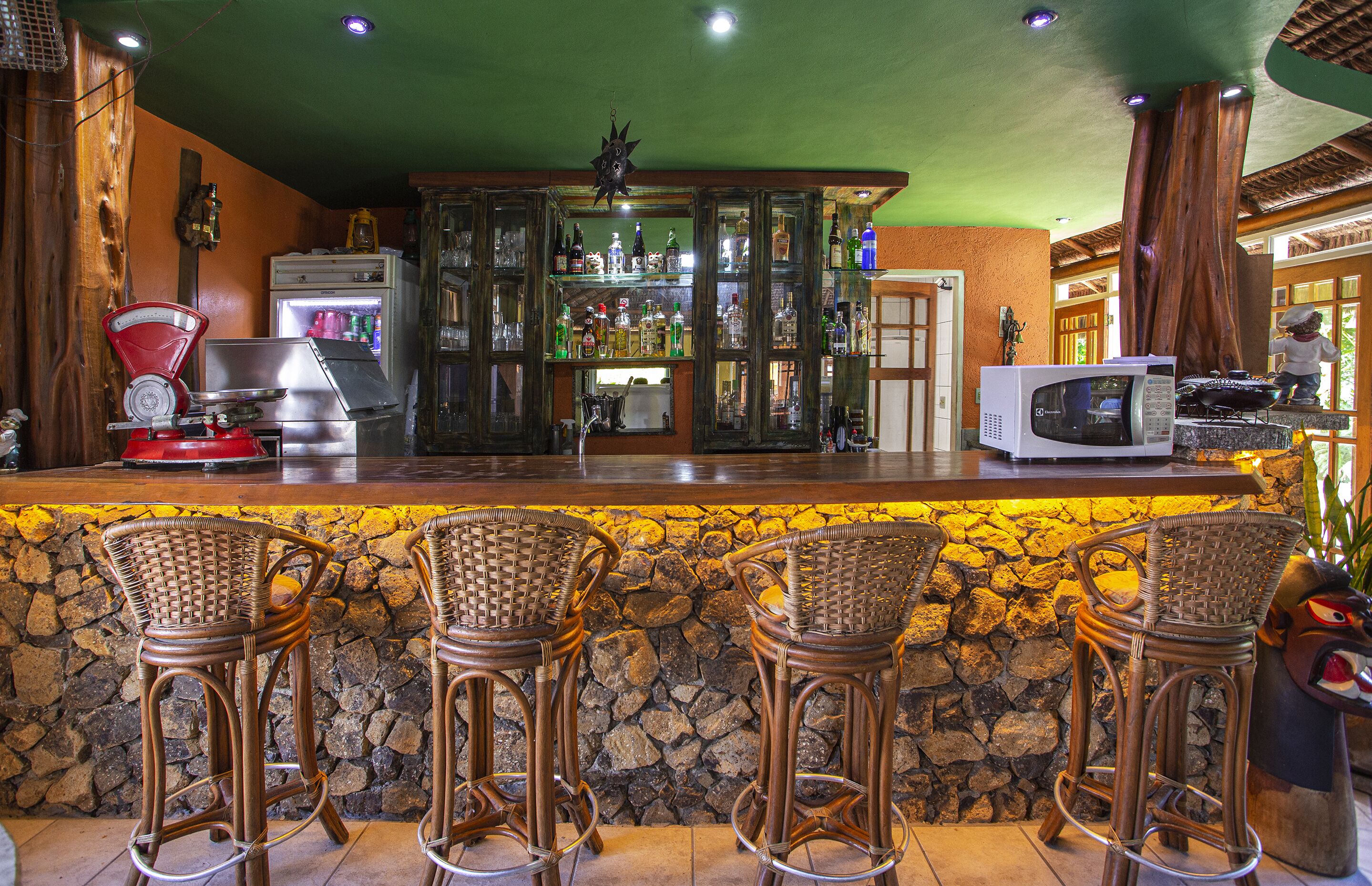 Eine Bar mit einer Steinwand, Korbsessel-Barhocker, einem Kühlschrank und einer Mikrowelle.