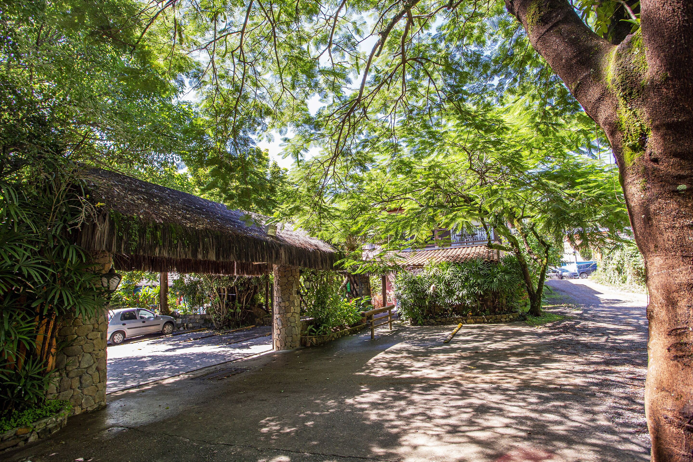 A covered outdoor area with a stone bench, a car parked nearby, and lush greenery.