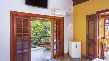 Um quarto com porta de madeira, um pequeno frigorífico branco e uma televisão montada na parede.