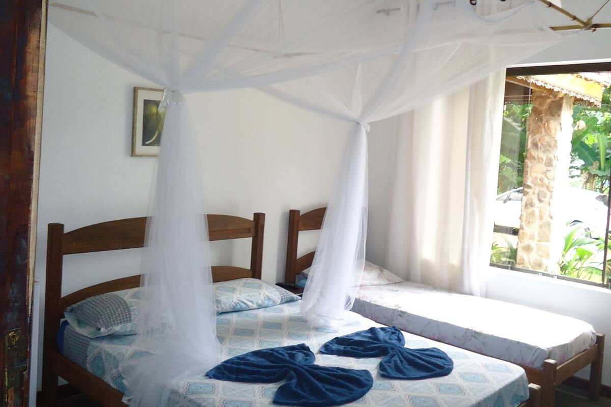 A room with two beds, each with a canopy bedspread and a white mosquito net.