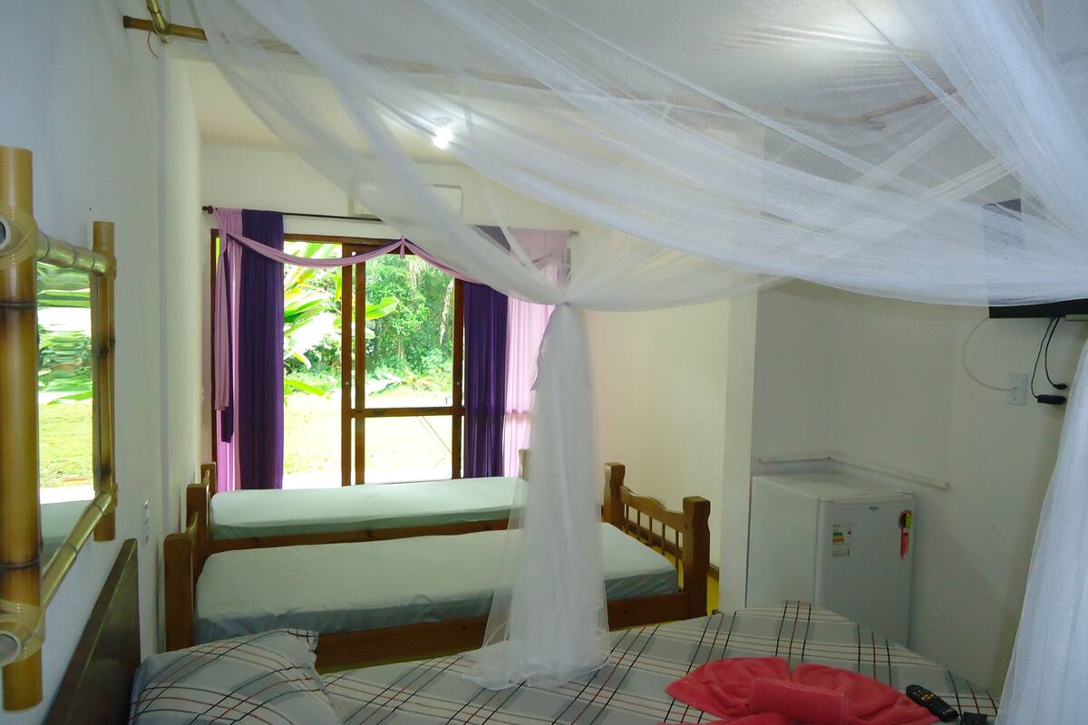 A room with a bed, a window with curtains, a mosquito net, and a bedside table.