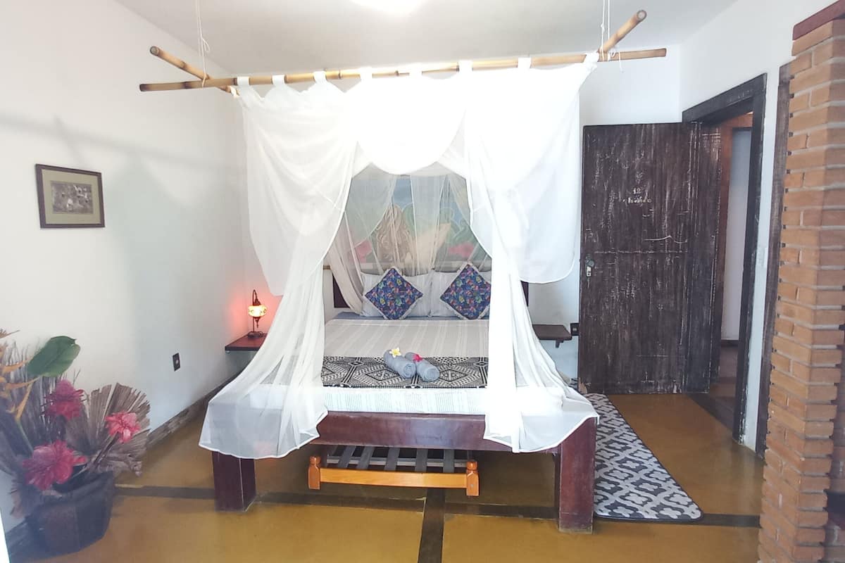 A bedroom with a bed under a white canopy, a bedside table with a lamp, and a brick wall.