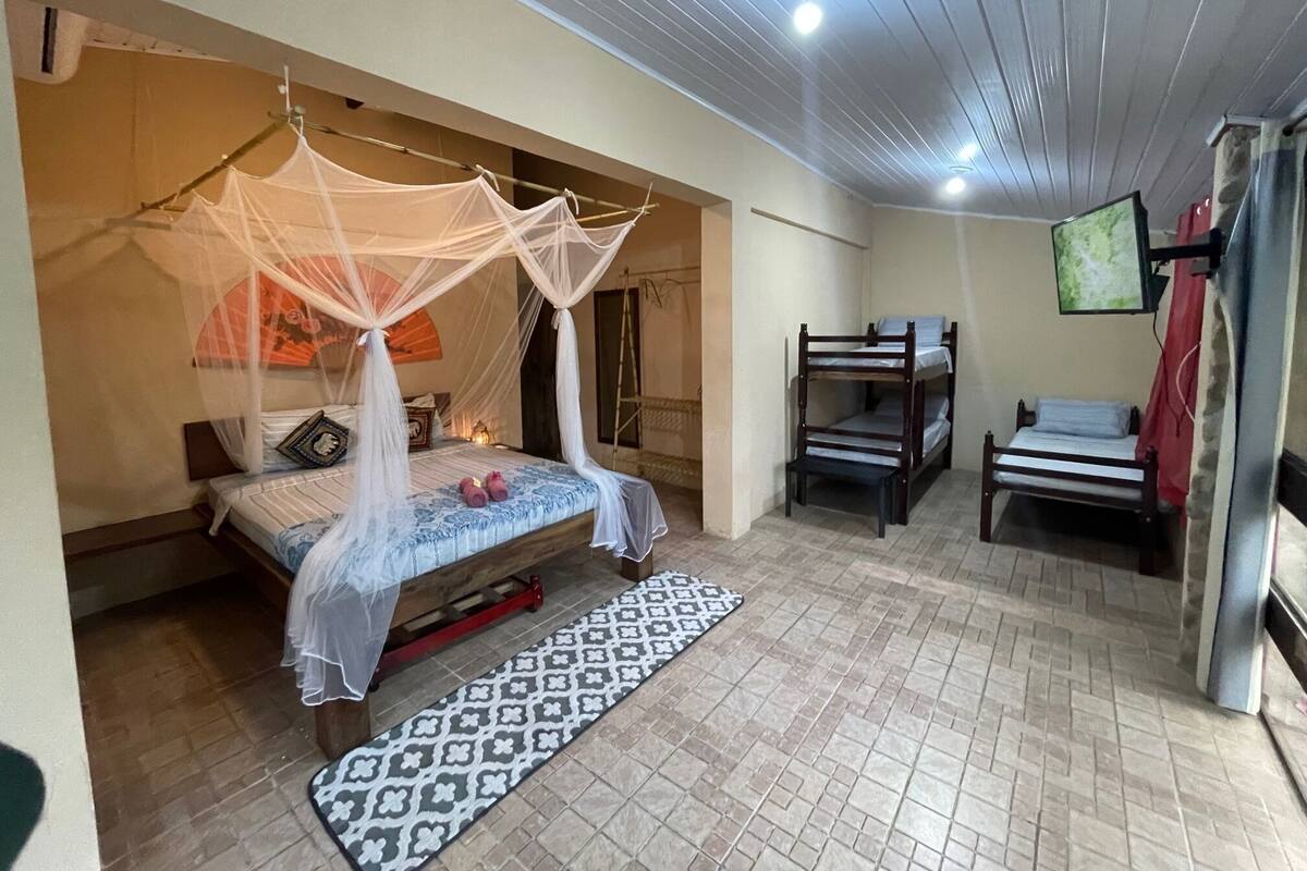 A room with a bed under a mosquito net, a bunk bed, a patterned mat, and a television on the wall.