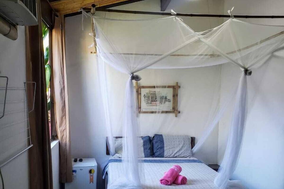 A small, cozy room with a bed under a mosquito net, a ceiling fan, and a small heater.