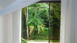 A room with a glass door leading to a garden with tropical plants. - Bali Suites Itamambuca (Ubatuba)