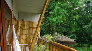A hammock on a wooden deck with a bamboo railing, surrounded by greenery. - Bali Suites Itamambuca (Ubatuba)