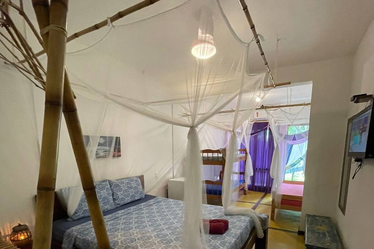 A room with a bed under a mosquito net, a bedside table, and a small stool.