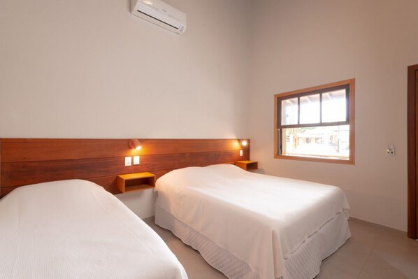 A bedroom with two single beds, wooden headboard, bedside lamps, and a window with a view.