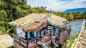 Un edificio de dos pisos con techo de paja, balcones con barandillas de hierro forjado y vista al océano.