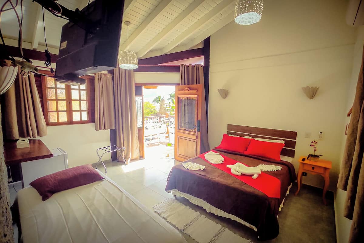 A bedroom with a bed, a wooden headboard, a nightstand, a desk, a chair, a television, and a window with curtains.