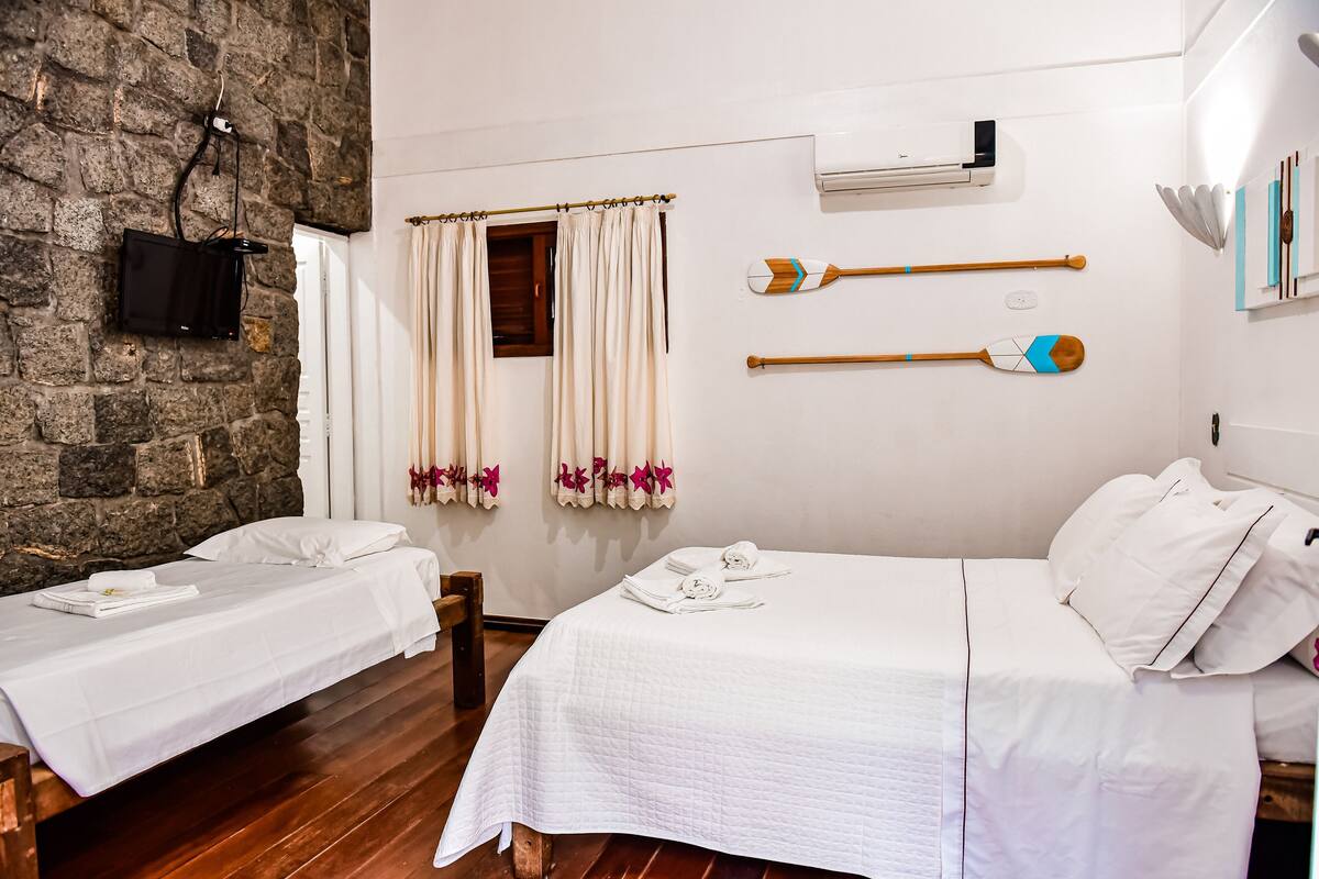 A hotel room with two beds, a stone wall, a flat-screen TV, and a window with curtains.