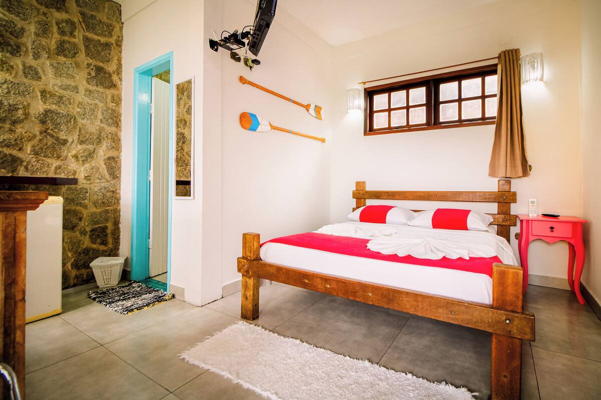 A bedroom with a wooden bed, a stone wall, a blue door, and a window with curtains.