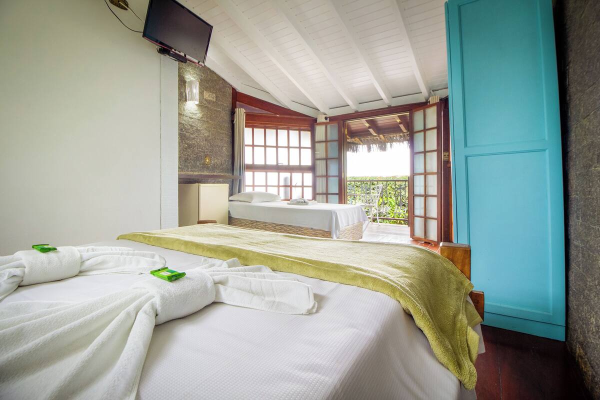 A hotel room with a bed, a massage table, and a view of greenery through a window.
