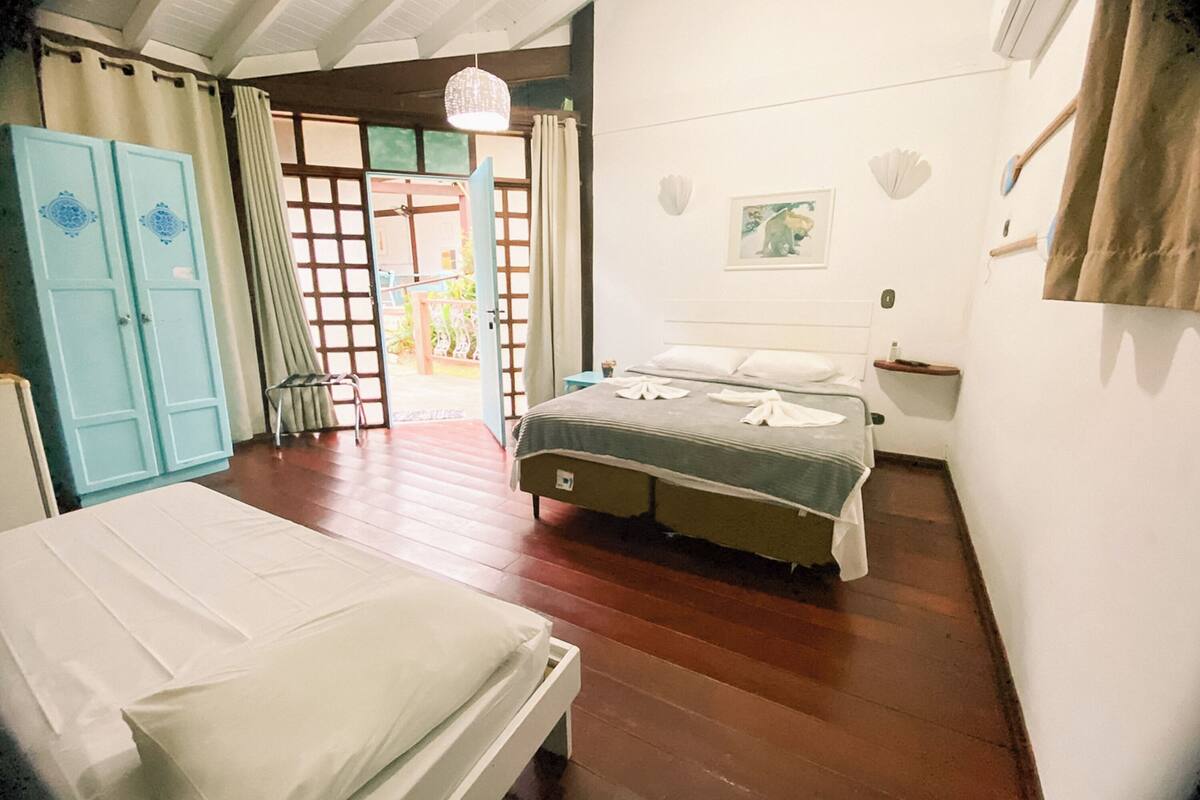 A bedroom with two beds, a wooden floor, a wardrobe, a door leading outside, and a wall-mounted shelf.