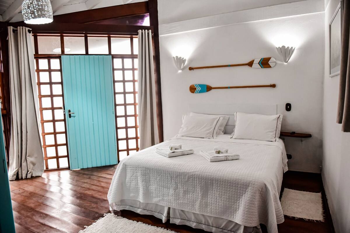 A bedroom with a bed, pillows, a bedside table, a wooden headboard, a wall-mounted decorative item, and a door with a grid pattern.