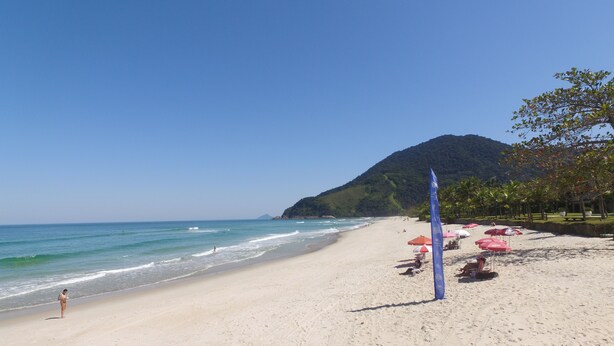 Una playa con cielo despejado, orilla arenosa y una montaña al fondo.