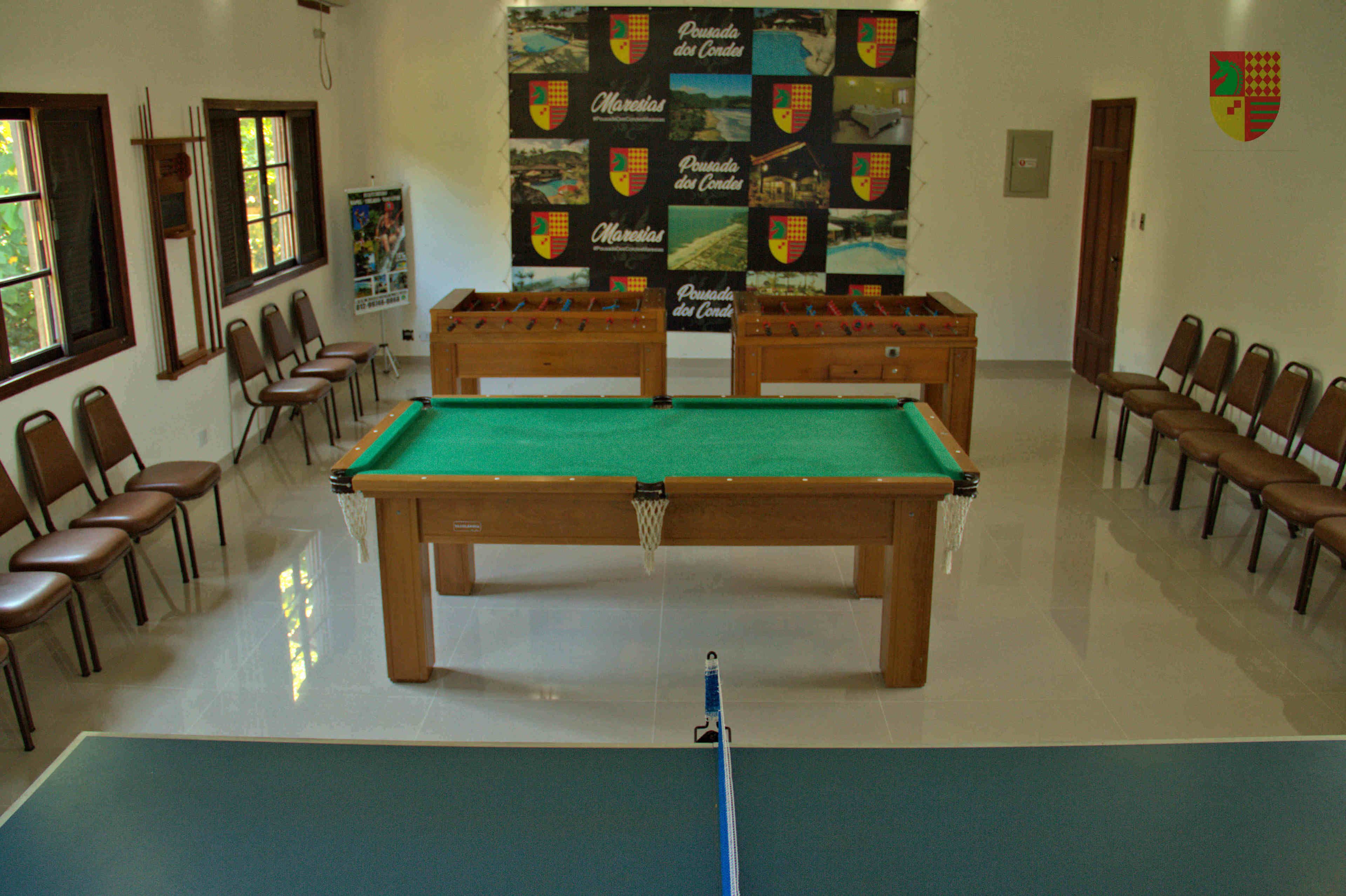 Une table de billard entourée de chaises, une affiche accrochée au mur et une porte au fond.