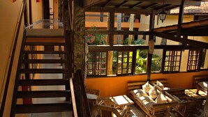 Una escalera de madera conduce a una habitación con vistas al exterior. Hay camas de madera y una mesa en la habitación.