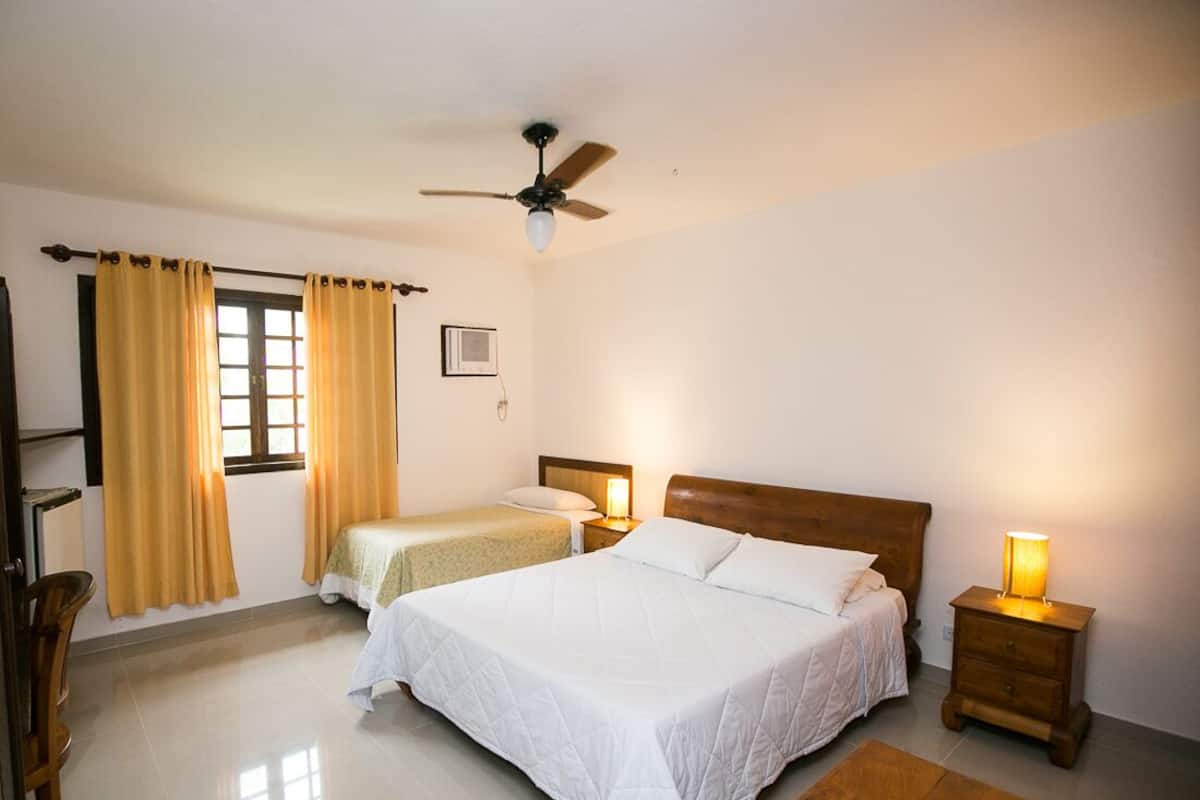 A bedroom with a large bed, two bedside tables with lamps, a ceiling fan, and a window with curtains.