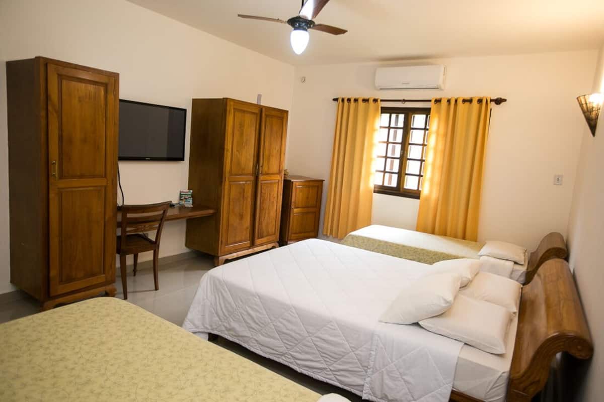 A room with two beds, wooden furniture, a desk, a television, and an air conditioning unit.