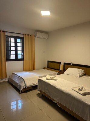Habitación de hotel con dos camas individuales, una ventana con cortinas, un equipo de aire acondicionado y una lámpara de noche.