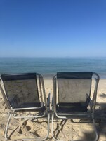 Two metal beach chairs facing the ocean.