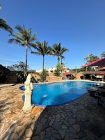 Una piscina con baldosas de piedra, palmeras y una estatua de piedra.