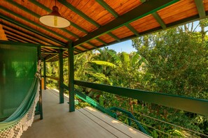 A wooden deck with a hammock, a green railing, and a view of lush tropical vegetation. - Pousada Ecoilha (Ilhabela)