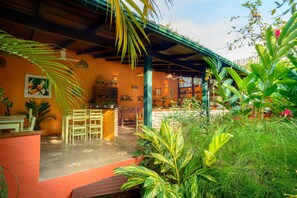 A covered outdoor area with a wooden table and chairs, surrounded by lush greenery and a variety of plants. - Pousada Ecoilha (Ilhabela)