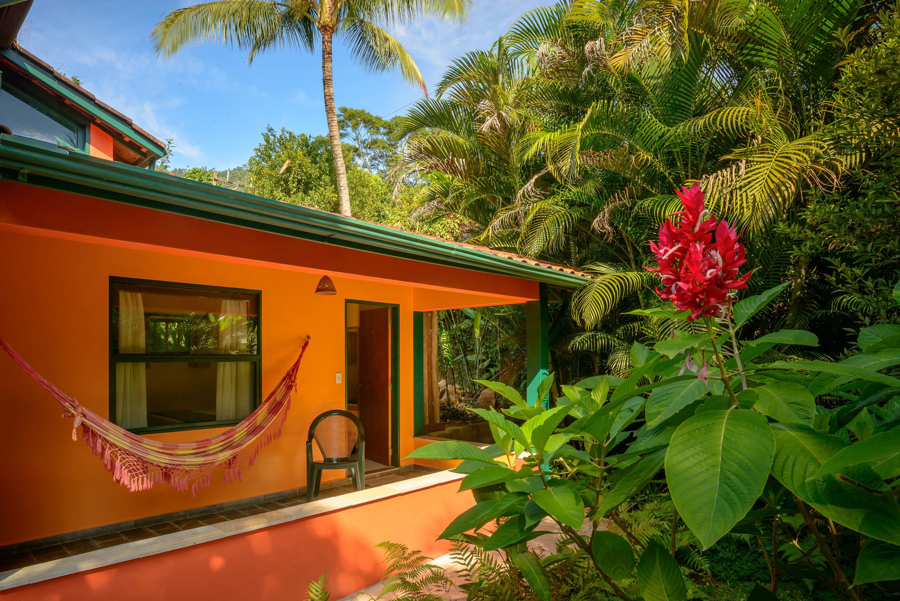 Een huis met een oranje gevel, een hangmat en weelderig groen.