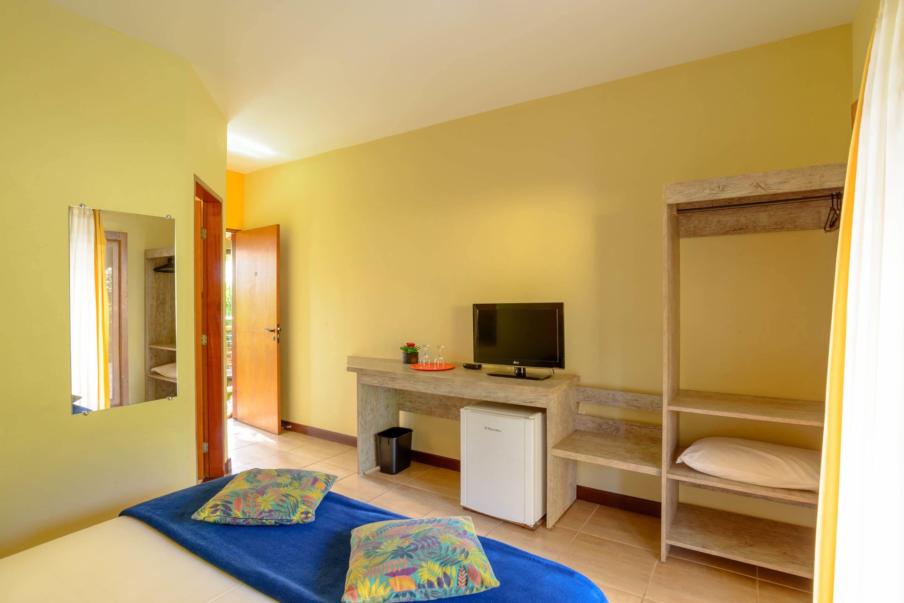 A room with a bunk bed, a desk with a TV, a small refrigerator, and a window with curtains.
