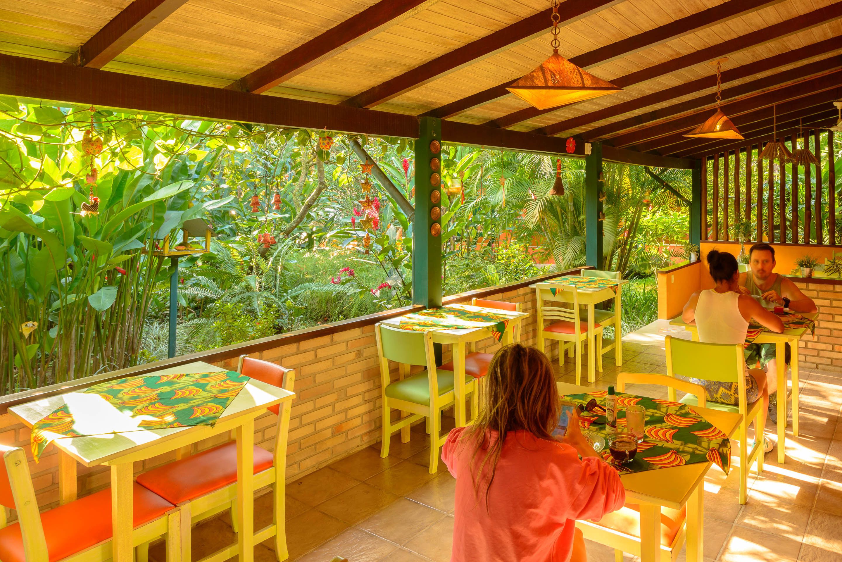 A restaurant with outdoor seating, surrounded by lush greenery and a wooden ceiling.