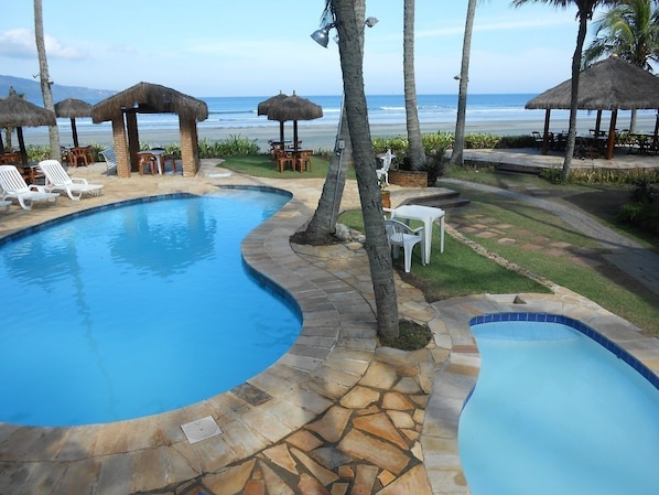A pool area with two separate pools, lounge chairs, and umbrellas. - Barequeçaba Praia Hotel (São Sebastião)